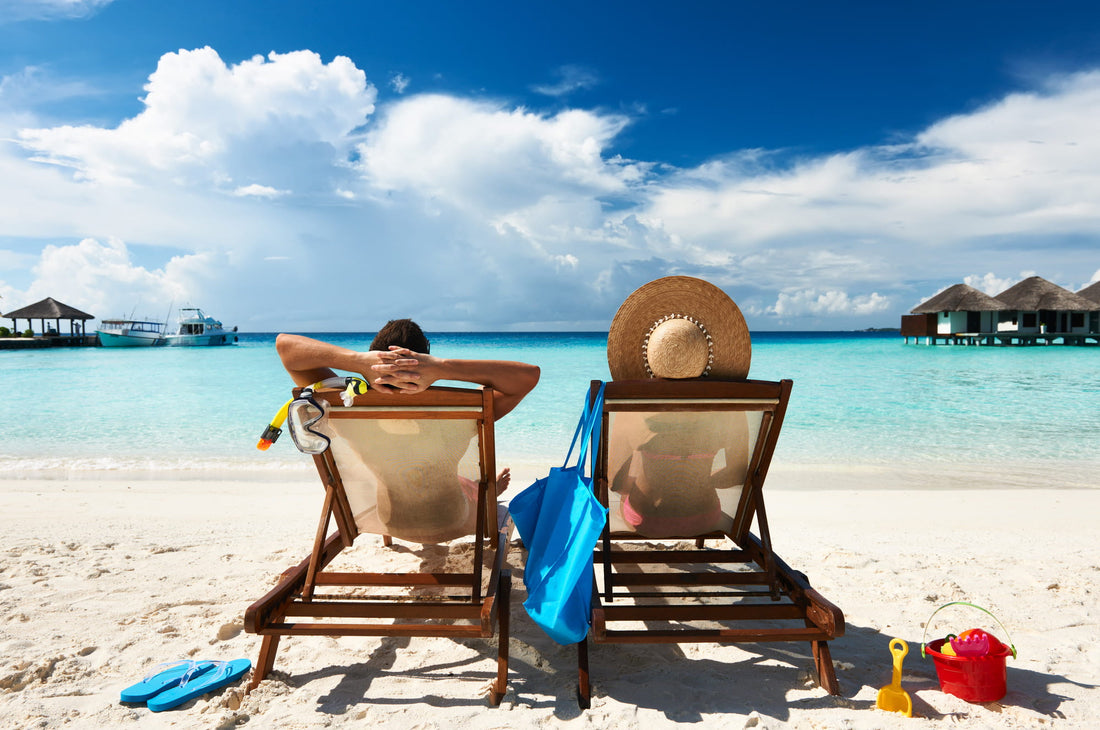 Two people vacationing on a beach lounging in chairs on the sand.