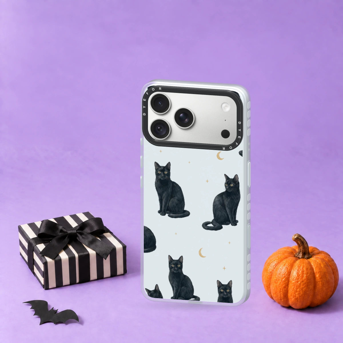 Moonlit Mews on the latest DYEFOR case render beside a black-bow striped gift and pumpkin on a lilac studio surface